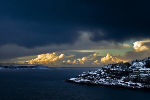 Houses on the snowy shore against the background of huge clouds