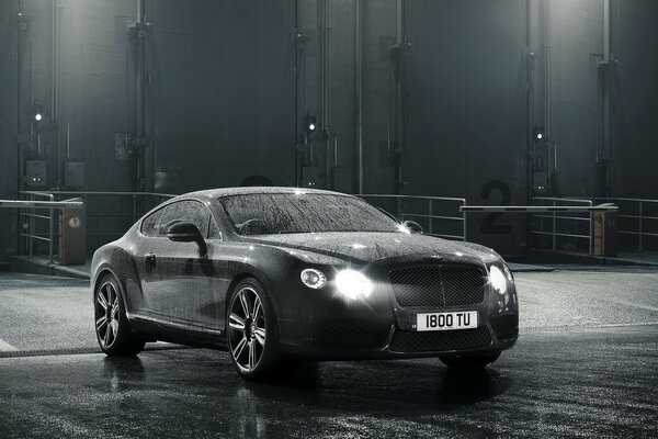 The car is standing on the sidewalk in the rain. At night