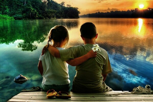 A boy and a girl hugged on the riverbank and look at the sunset