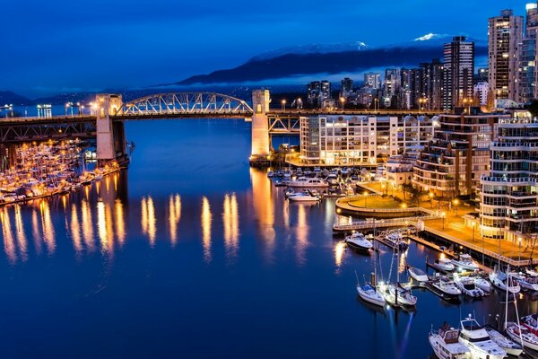 A bridge across the river connecting parts of the night city in lights against the background of a mountain in a white fog