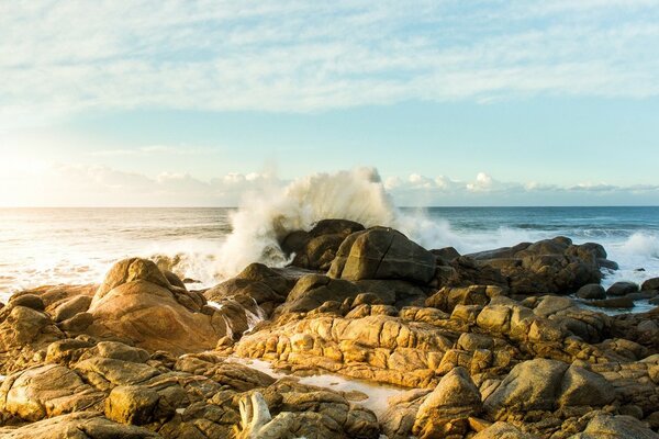 A wave crashing against large rocks on the shore