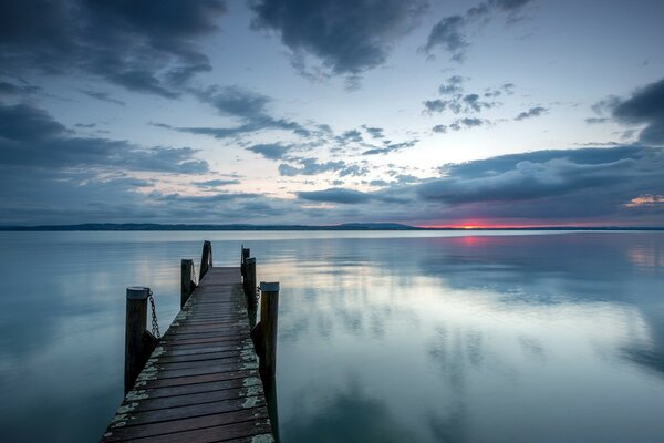 A narrow bridge goes into the lake at sunset