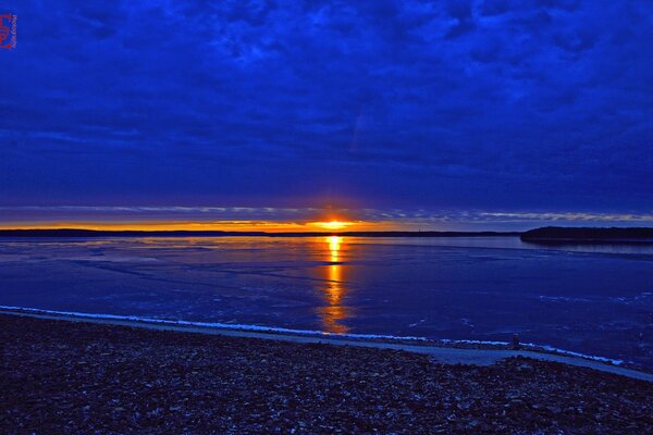 Rich blue clouds covering the setting sun over the lake